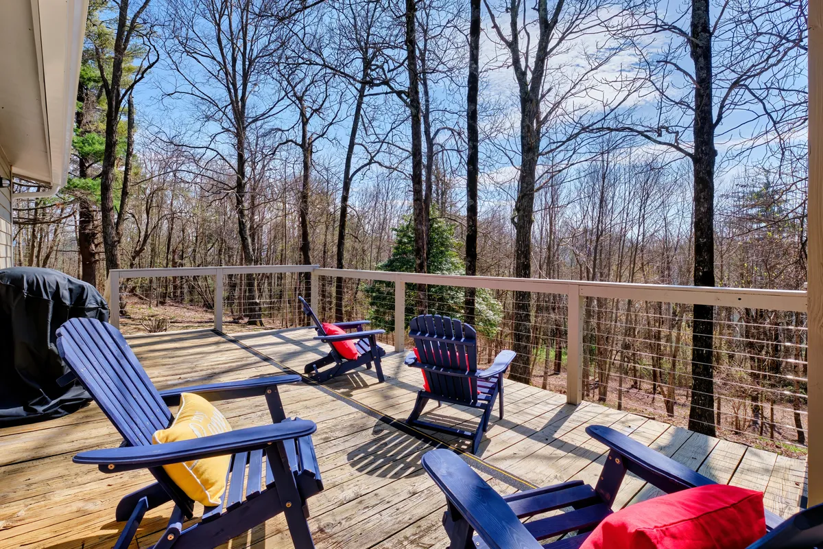 An inviting wooden deck outfitted with Adirondack chairs, overlooking a serene forest backdrop. The space is open to nature, ideal for relaxing, enjoying a meal outdoors, or simply soaking up the mountain air and sunset views.