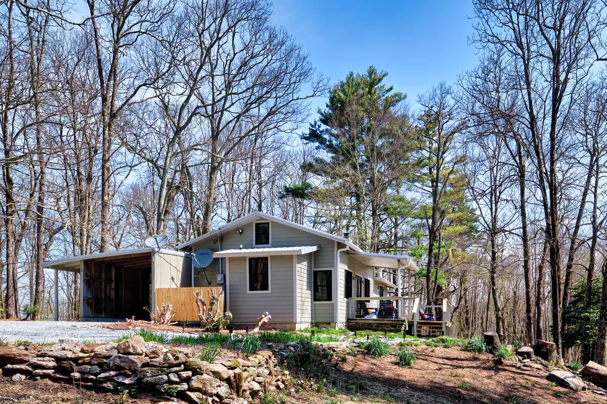 A serene exterior view of the home with its covered porch (lanai) nestled among mature trees and vibrant flower beds. The porch appears inviting for relaxation, framed by nature and offering a peaceful retreat with sweeping views.