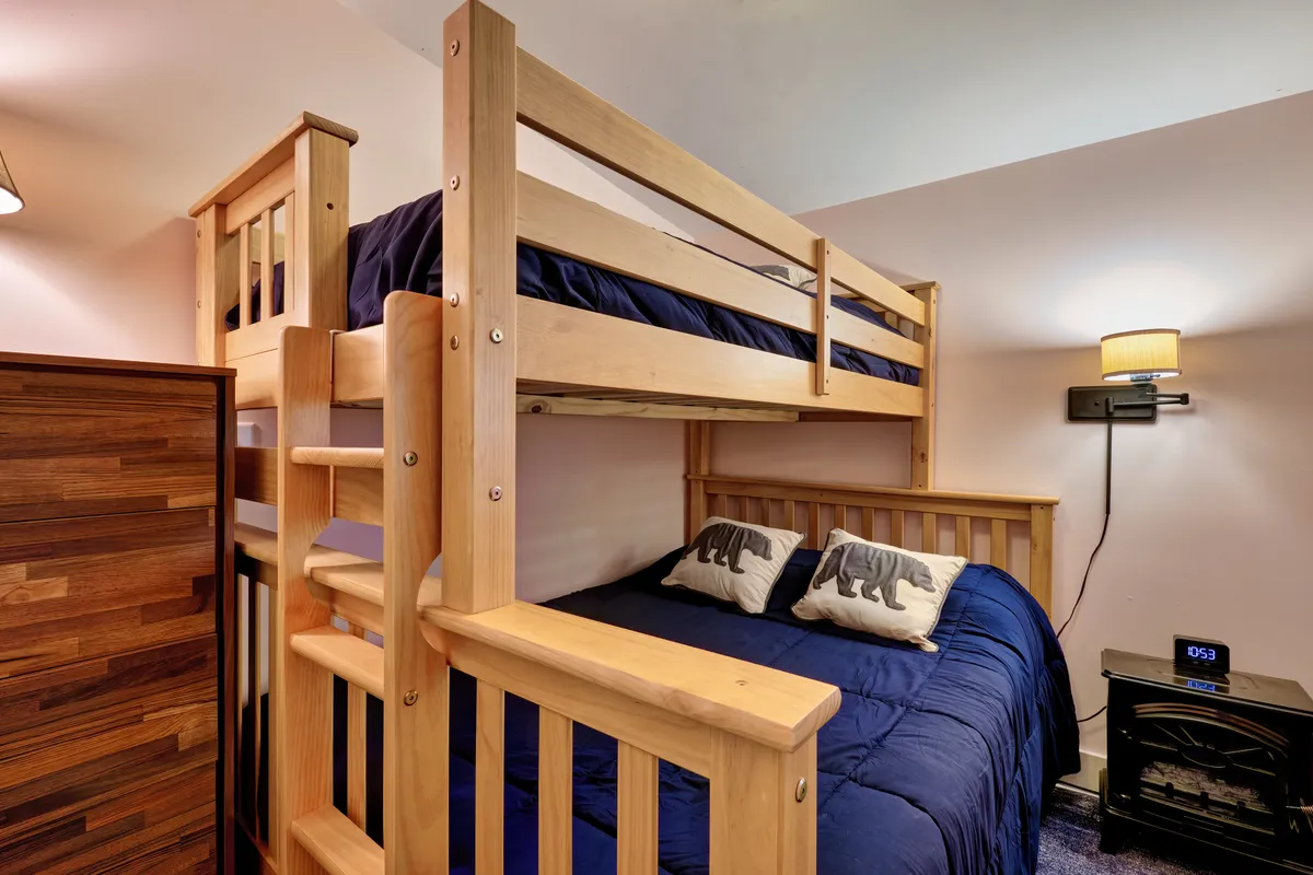 A warm, lofted bedroom space with a neatly made bed, decorative pillows, and wooden furniture. The inviting bedding and intimate scale suggest a perfect setting for family bonding, reading stories before sleep, or enjoying quiet moments together.