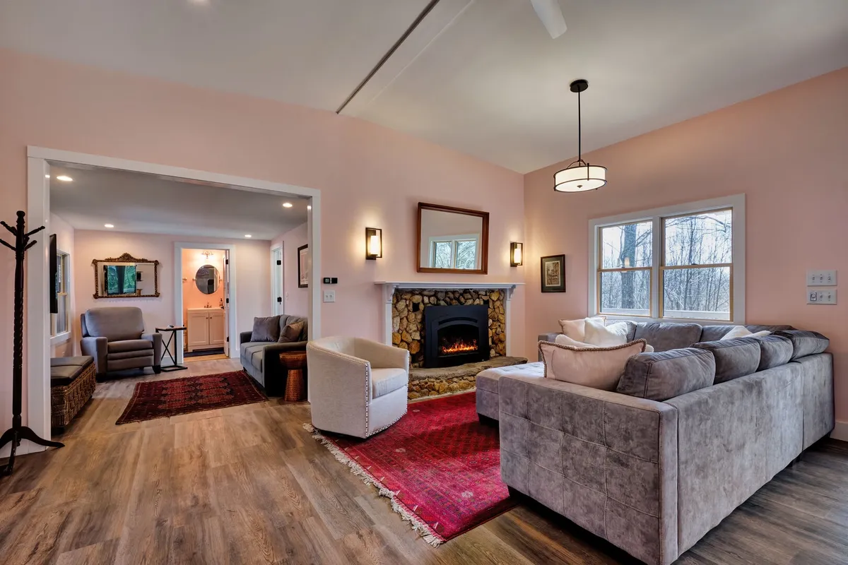 The image showcases a warm, inviting living area with plush sofas arranged around a glowing fireplace, a soft rug underfoot, and an ambiance perfect for gathering and unwinding. The space is filled with natural light, offering a cozy haven for guests to relax, read, or enjoy time together, embodying the property's mountain charm and comfort.