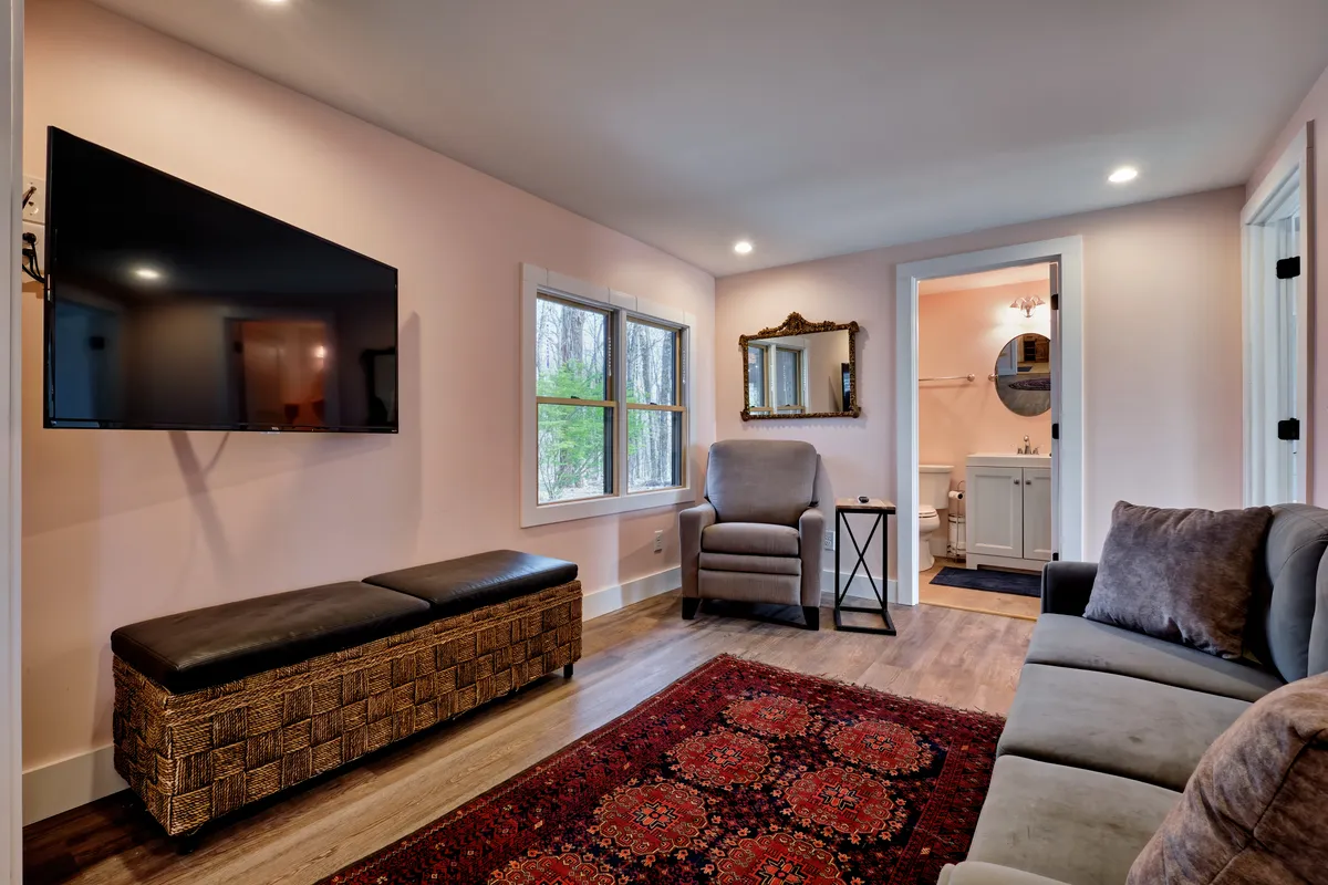 A cozy living area with a comfortable seating arrangement, a television mounted on the wall, a decorative mirror, and a soft rug. The space is inviting and ideal for gathering, relaxing, watching movies, or playing games with family and friends.