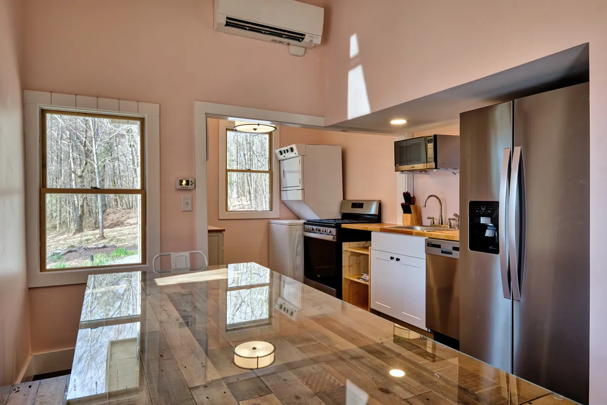 This image showcases a spacious, welcoming kitchen featuring a central island, modern appliances, and a large window that brings in natural light. A wooden dining table is set nearby, suggesting a space that is ideal for both cooking and casual dining. The layout encourages togetherness, and the visible elements emphasize culinary creativity and shared meals.